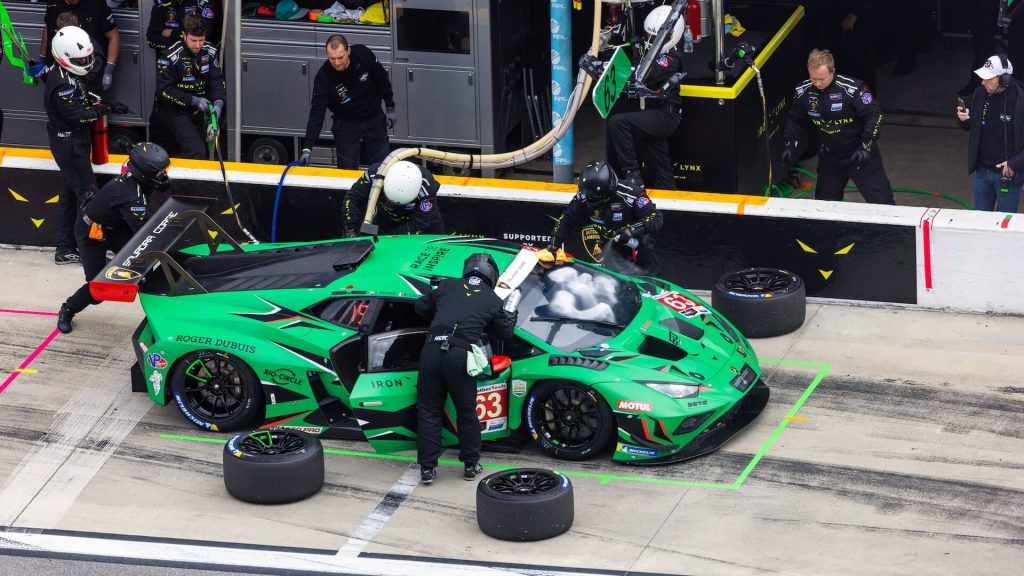 A green racing car in a pit stop area, where it's being serviced by the pit crew.