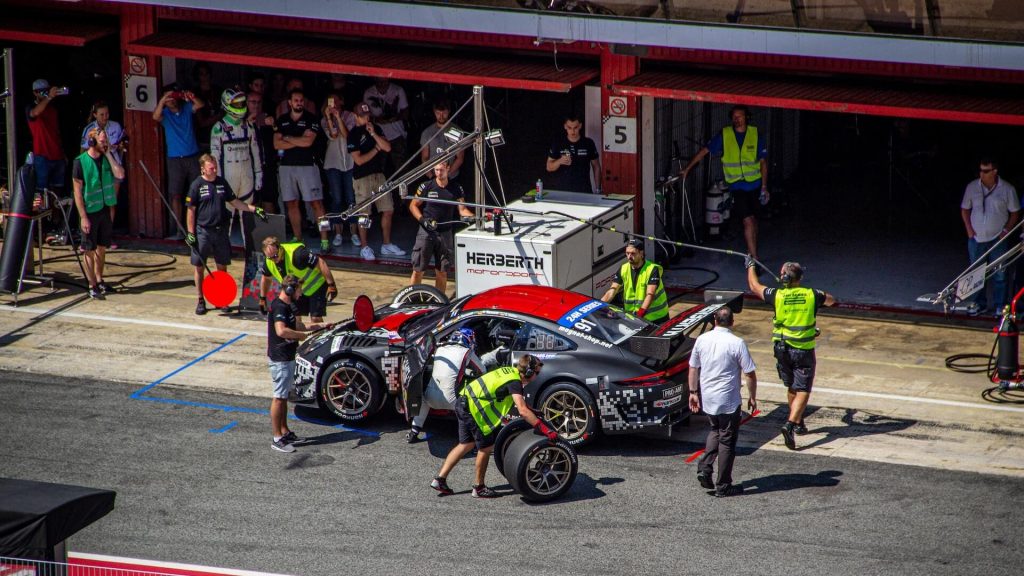 A grey racing car positioned at a pit stop for maintenance by the skilled pit crew.
